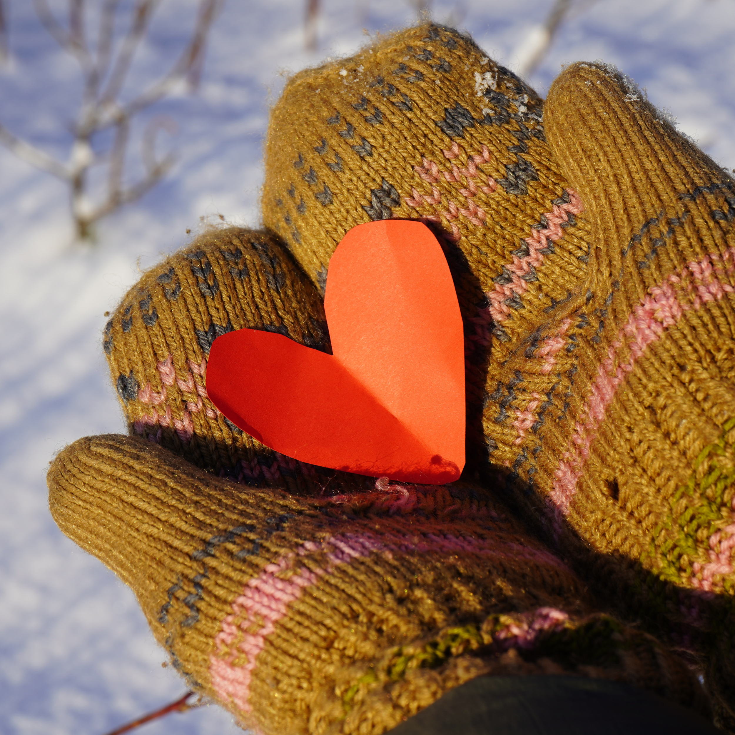 Hands wearing green and pink mittens hold out a red paper heart