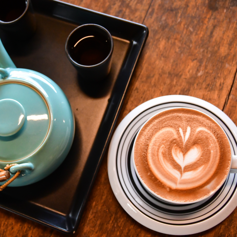 Teapot with small tea cups and a cup of coffee with cream in the shape of a heart