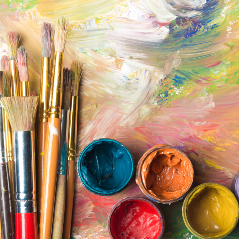 Paint brushes and paint jars filled with paint against a painted canvas background