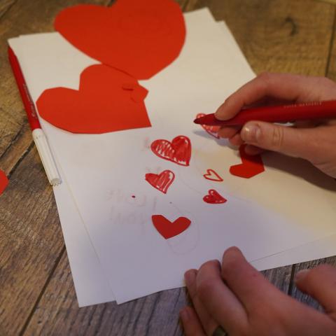 A craft project with bright red paper hearts on white paper