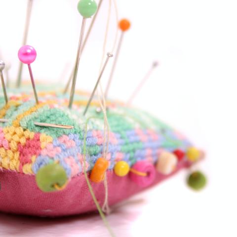 Multicolored pincushion with pink, green, and orange pins.