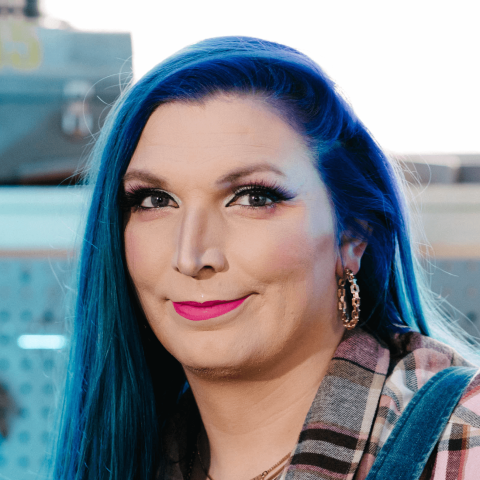 The author and presenter Mercury Stardust, a white woman with blue hair and pink lipstick, wearing overalls.