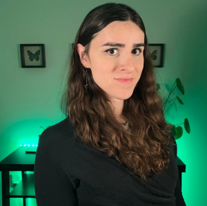 Erin Reed, a woman with long brown hair dressed in all black. The background is lit with a glowing green light.