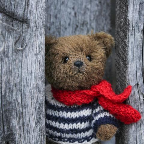 brown teddy bear in a knit sweater and red scarf