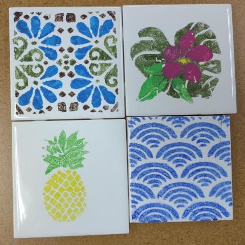 Four white tiles painted with geometric patterns or florals