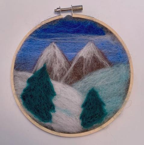 needle felted winter scene in embroidery hoop, showing trees, moutains, and snowy fields with a blue sky