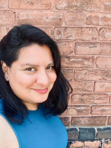 Isabel Marcheselli, smiling and looking directly into the camera. The background is a red brick wall.