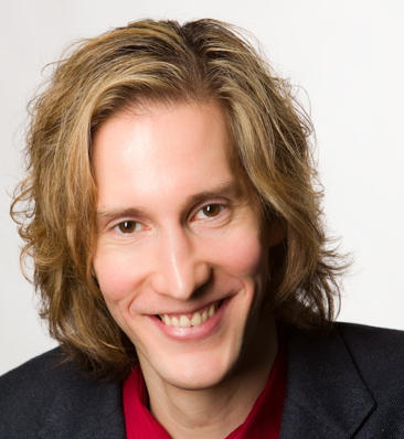 Keir White headshot. young white man, shoulder length blond hair, red shirt, black jacket