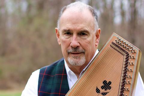 White man with wtie shirt and dark vest holding a musical instrument