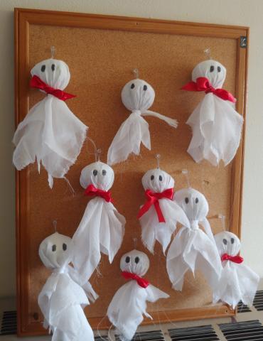 Tissue paper ghosts with red bow ties hanging from a bulletin board
