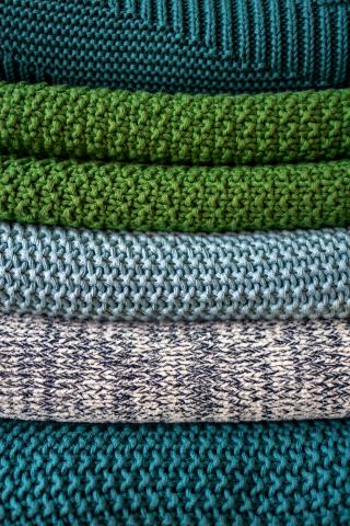 Pile of textured knit blankets in shades of green, blue, and gray