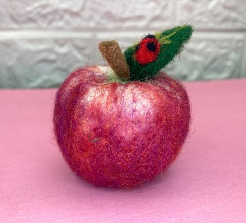Felted red apple with green leaf and brown stem on pink tabletop
