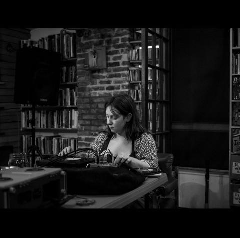 A black and white photo of a woman sitting at an audio mixer.
