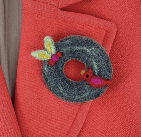 Felted dark green wool wreath with tiny holly and cardinal, pinned to red coat lapel