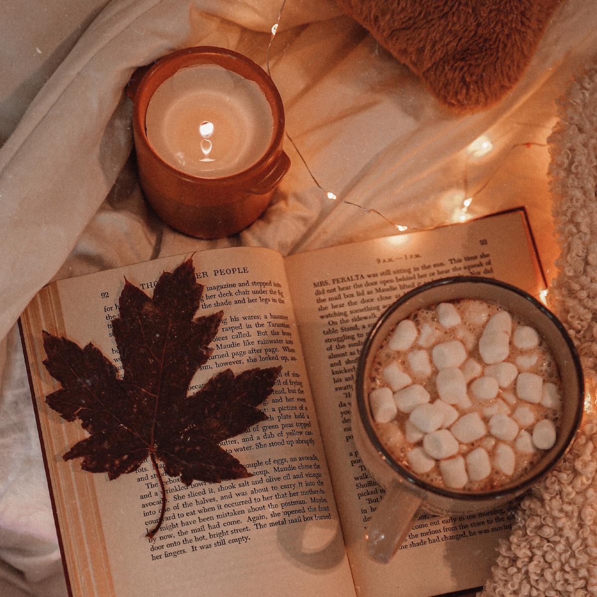 A cozy scene with a cup of cocoa, a maple leaf, and a book, lit by a candle