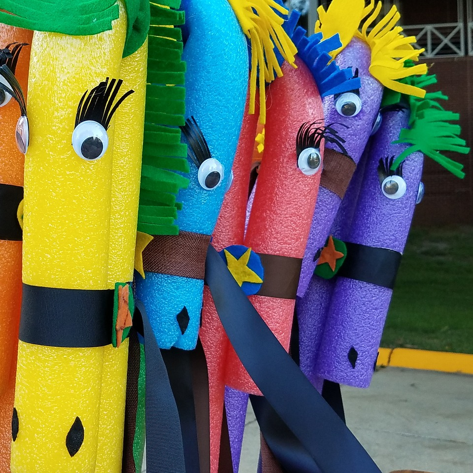 Colorful pool noodles with googly eyes and foam manes and eyelashes.