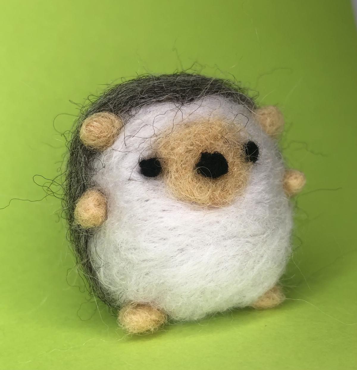 Felted brown and white hedgehog on green background