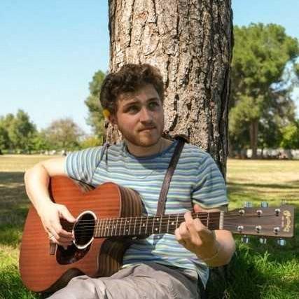 Guitarist Aaron Bogin sitting under a tree playing music.