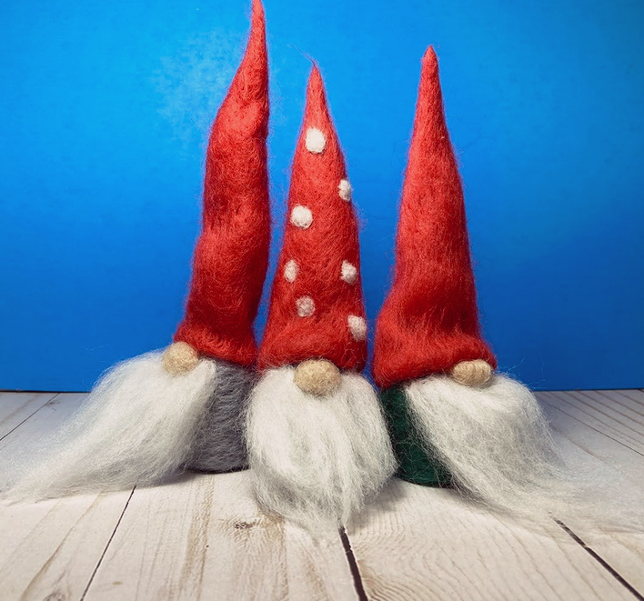 three felted gnomes with tall red hats on a wooden surface with a blue background