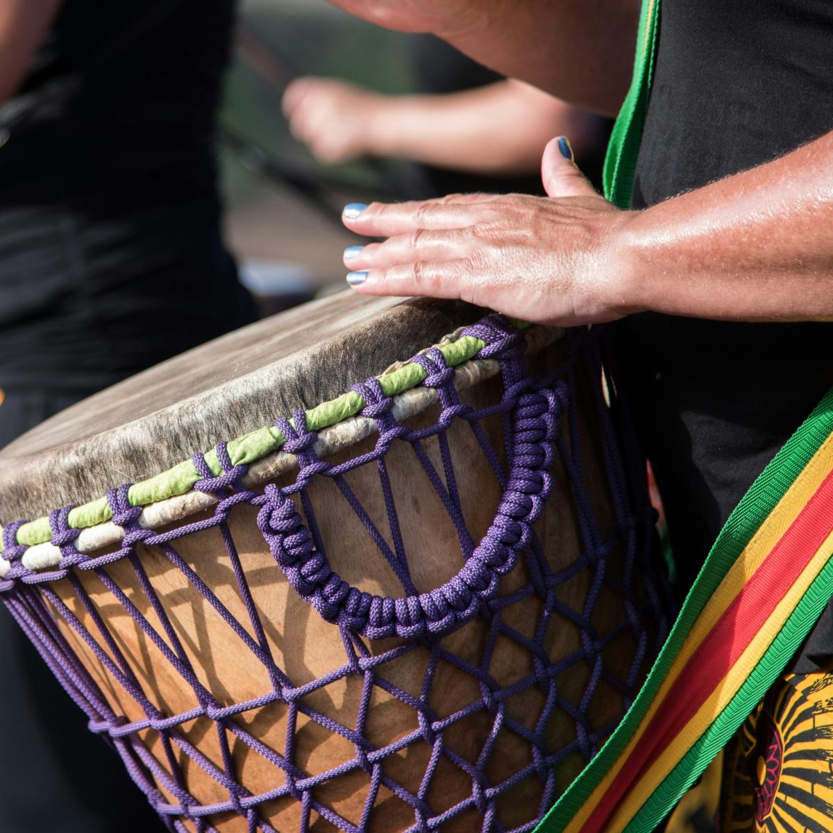 Hands drumming on a goblet drum wrapped in purple string