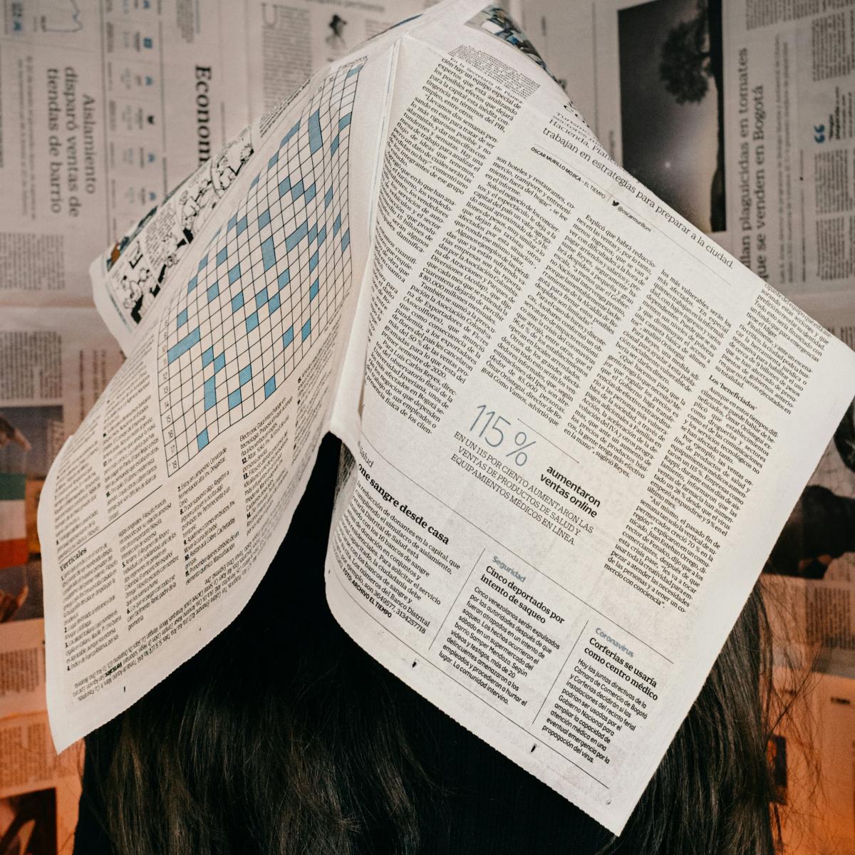 A person with long black hair with a newspaper over their face.