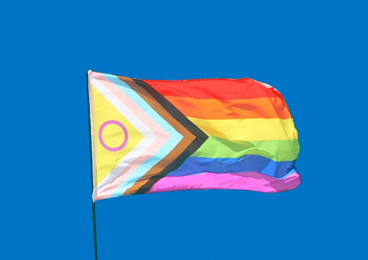 An intersex-inclusive progress pride flag flying against a bright blue sky