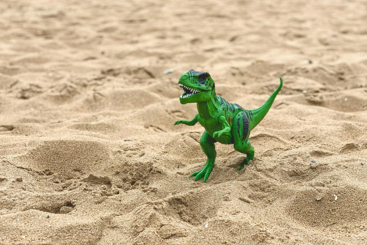 A bright green toy t-rex standing in the sand