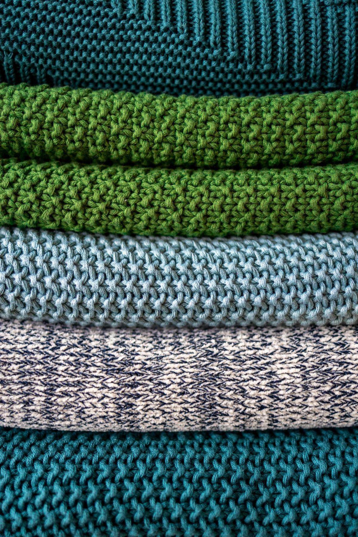 Pile of textured knit blankets in shades of green, blue, and gray