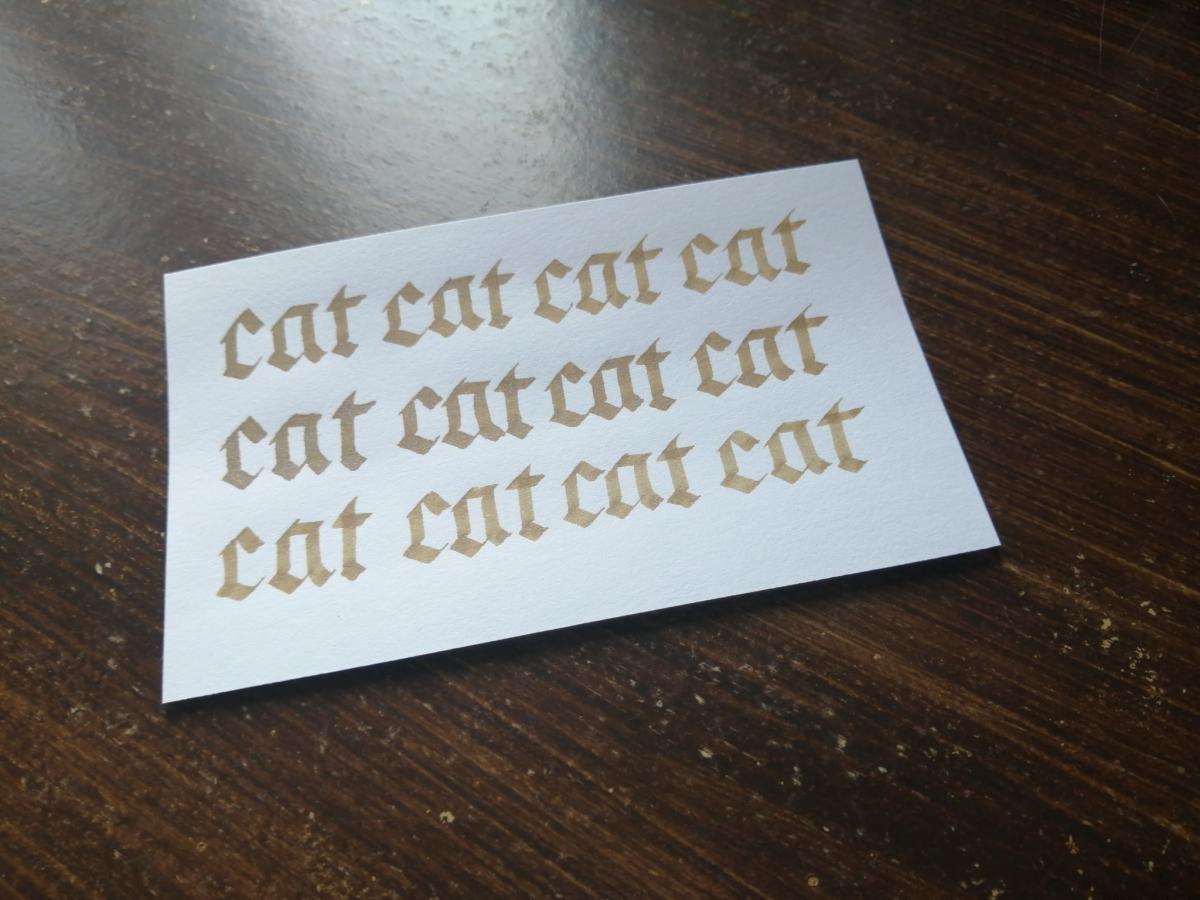 Blackletter calligraphy that says the word "cat" 12 times in gold ink