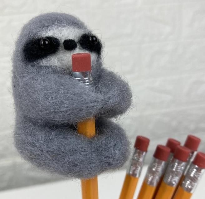 Felted gray sloth clinging to a yellow pencil